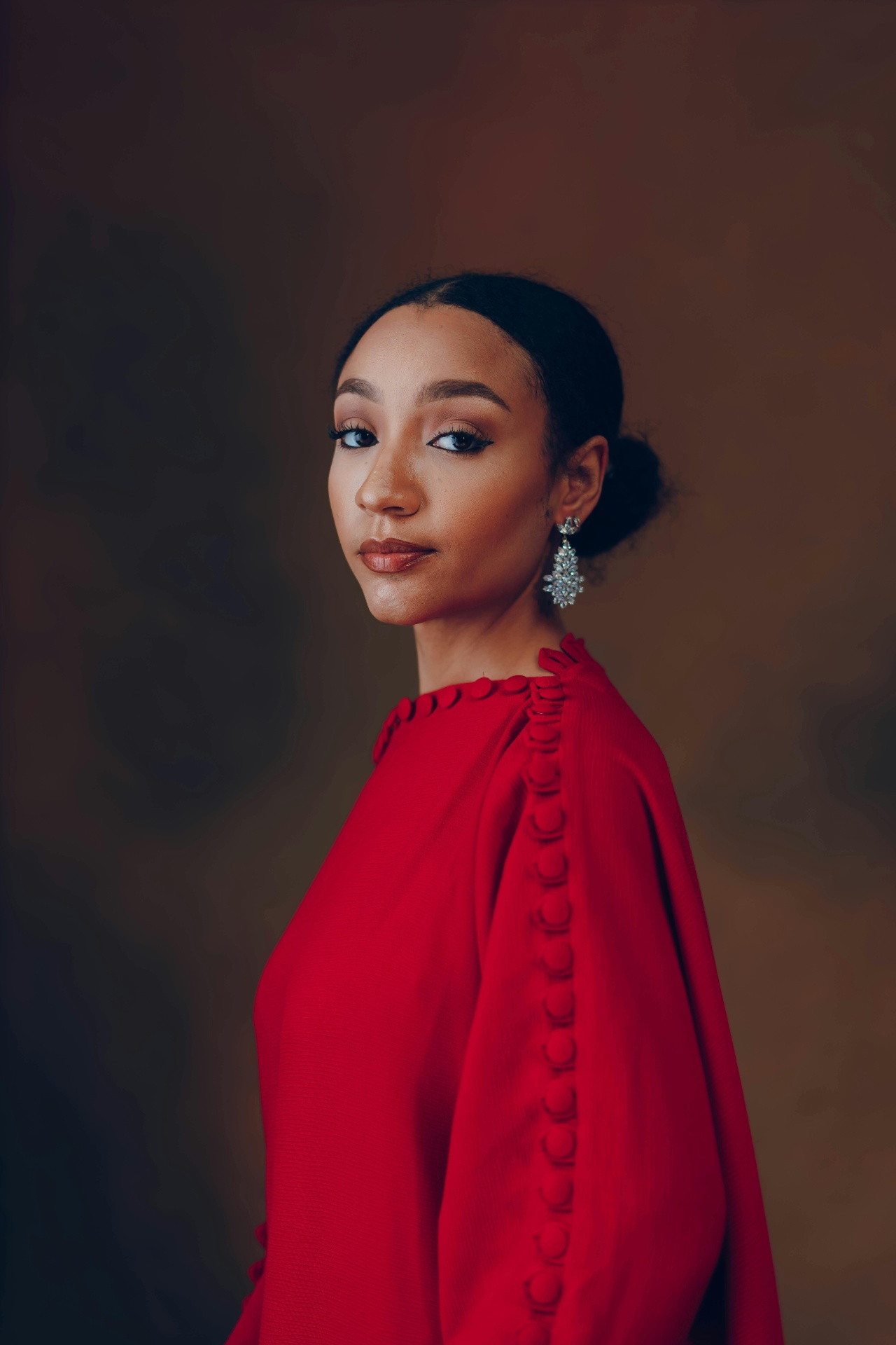 Studio portrait of a woman in a flowing red gown with crystal earrings against a warm backdrop