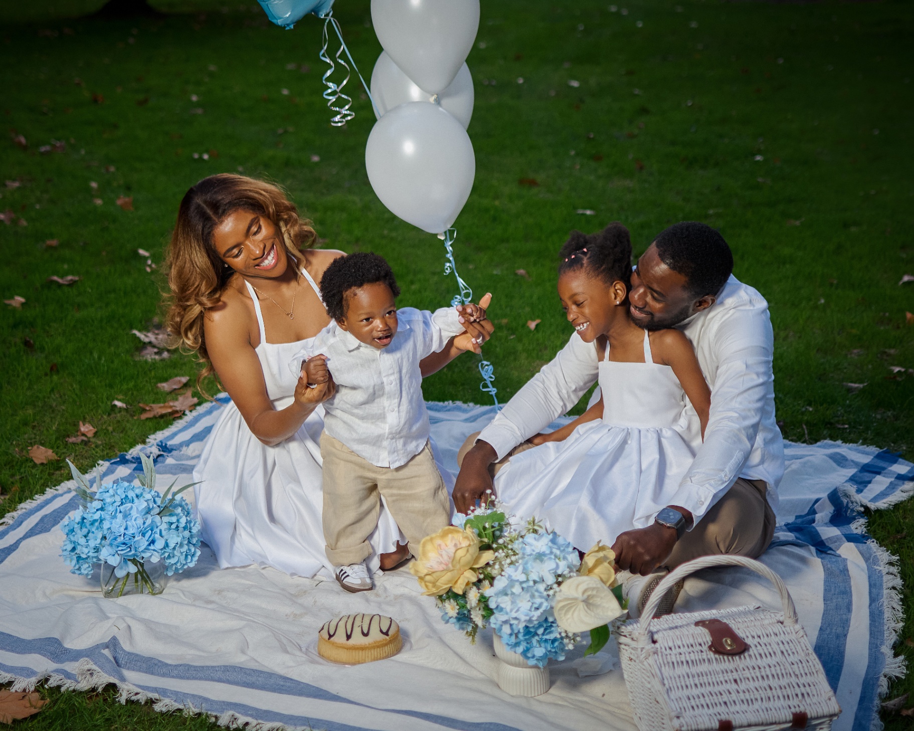 Joyful family picnic on a blue striped blanket with balloons and hydrangeas