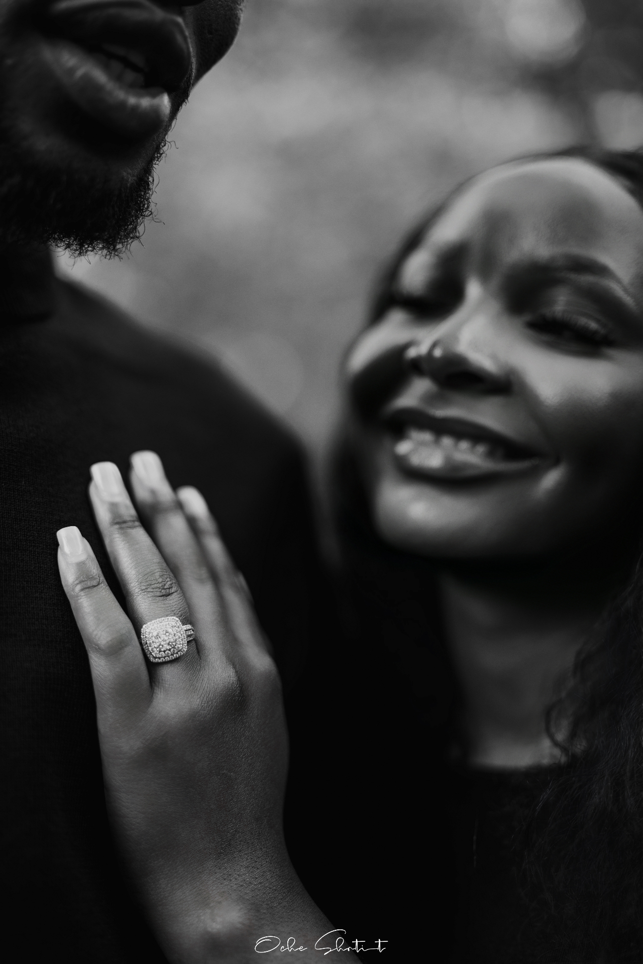 Black and white close-up portrait showing engagement ring on a smiling couple