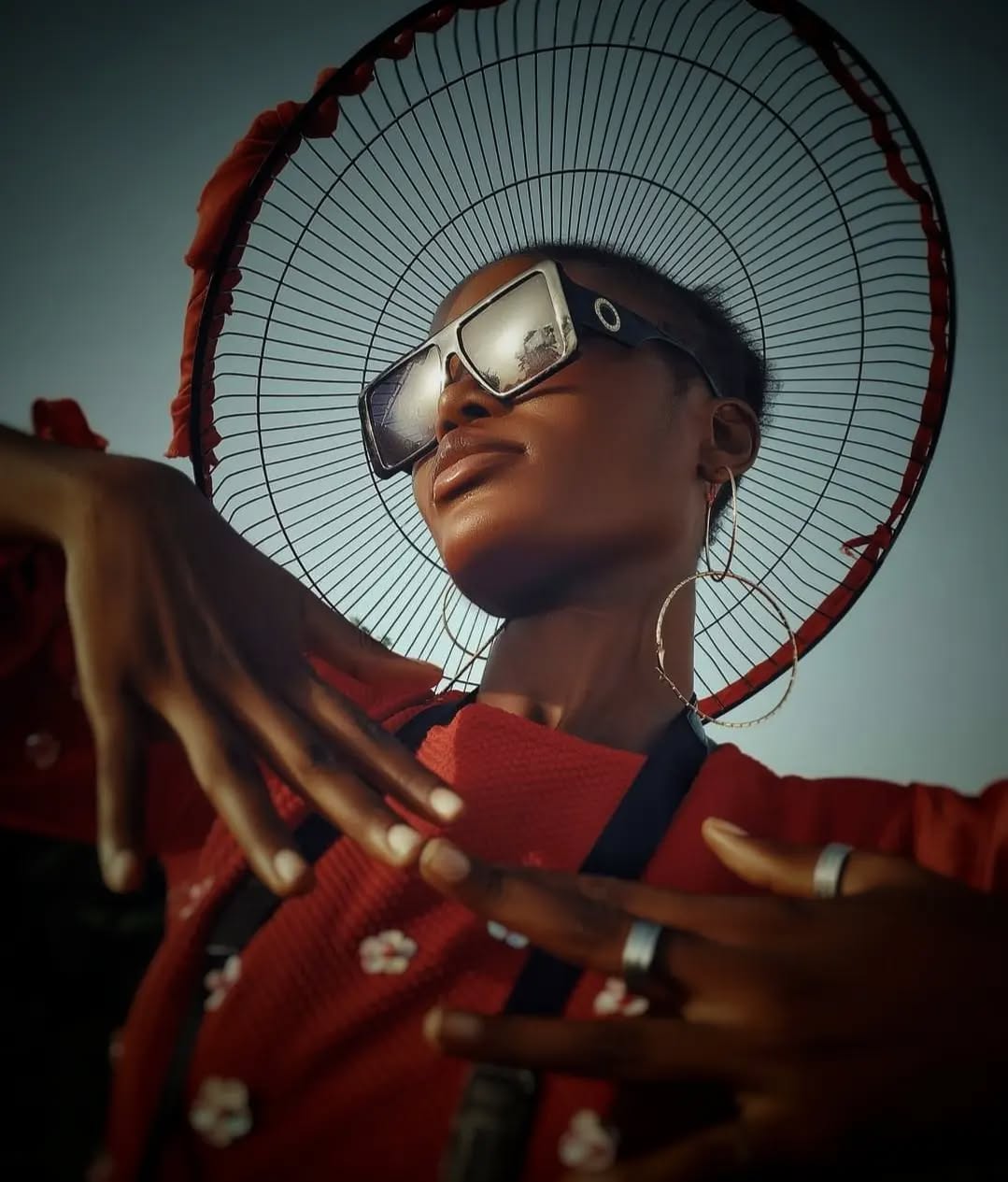 Striking low-angle portrait in red with oversized woven fan hat and mirrored sunglasses