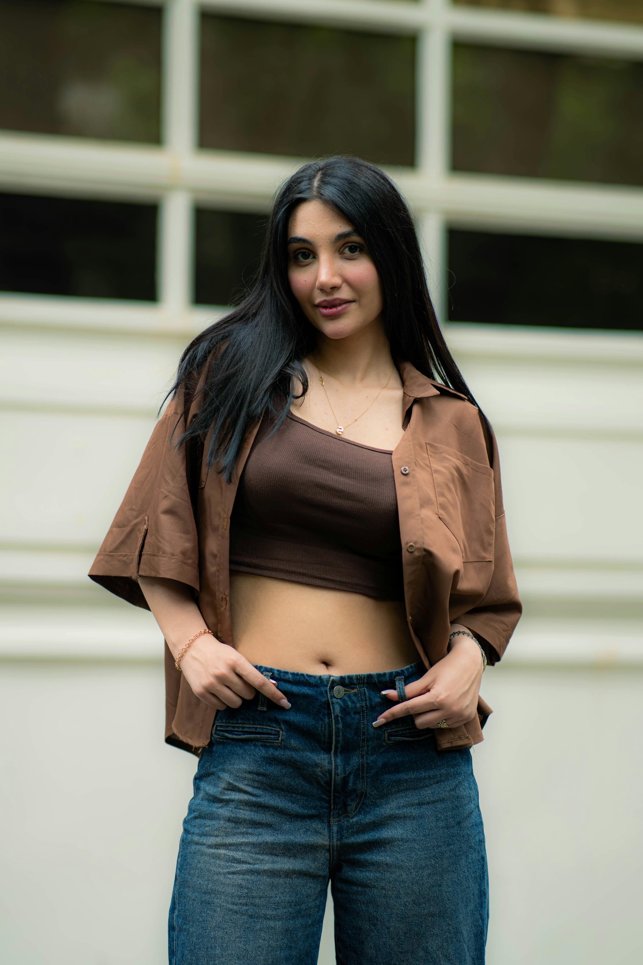 Portrait of a woman in an oversized brown shirt and brown crop top against a paneled wall
