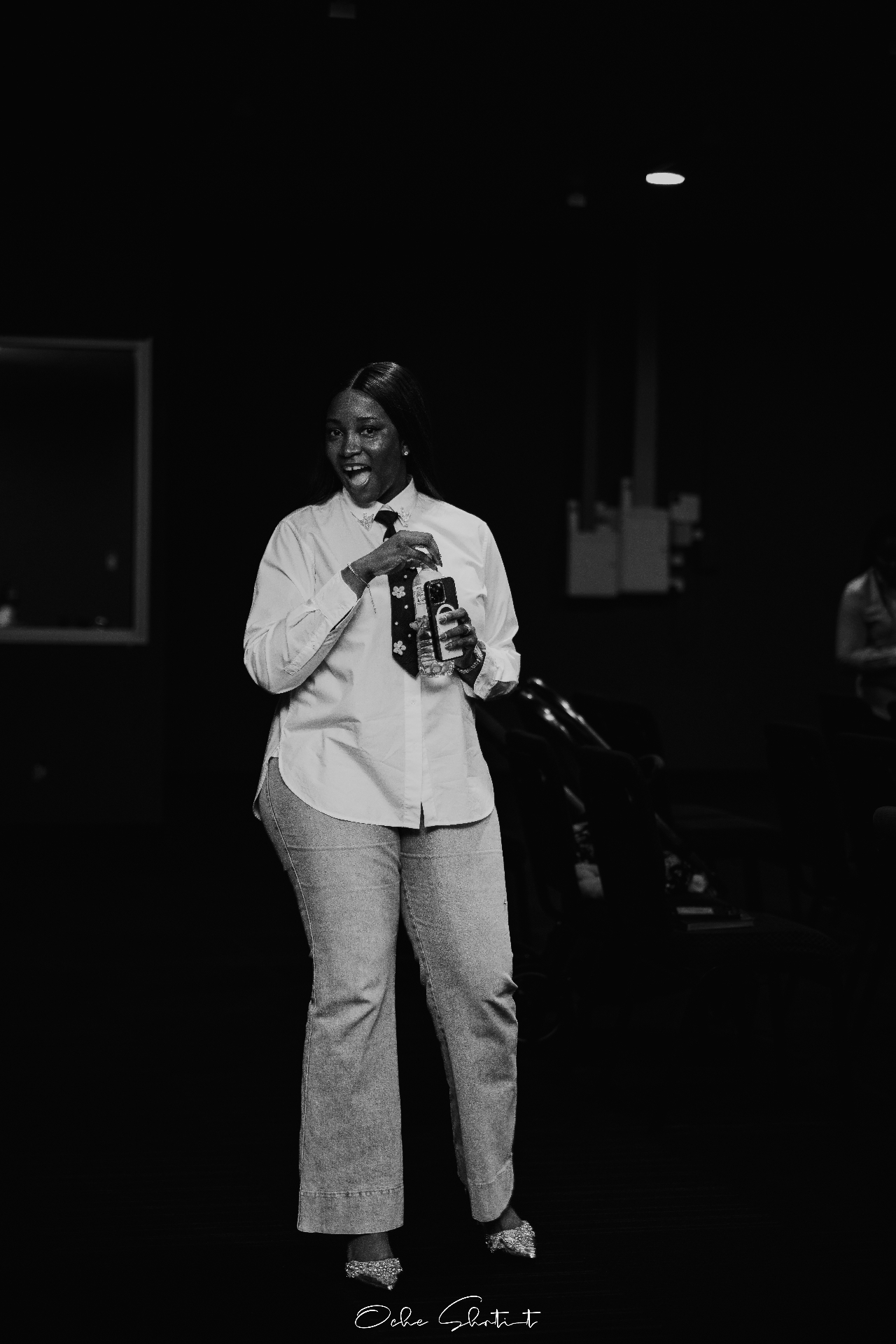 Speaker standing on stage holding phone, dramatic low light
