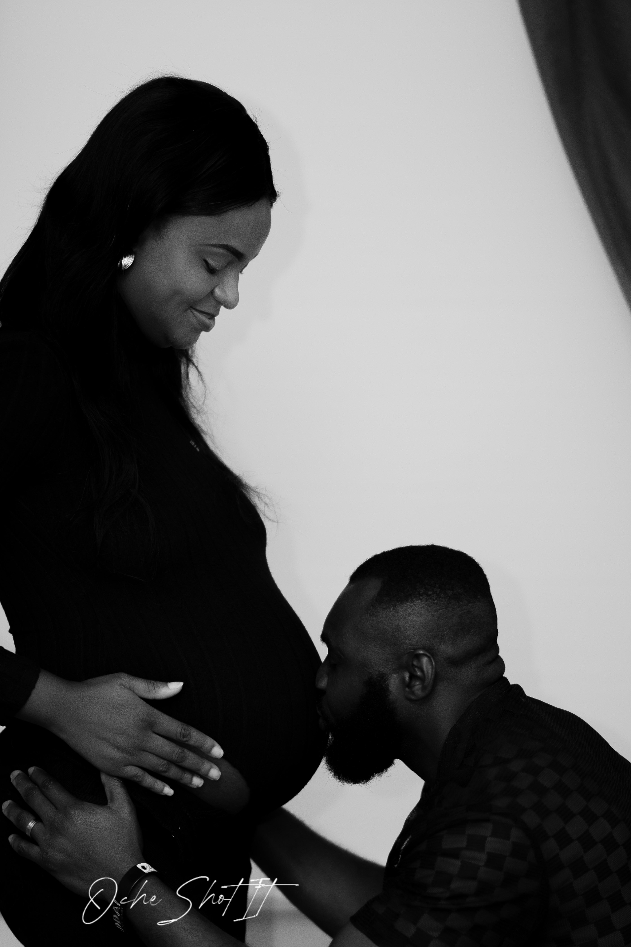 Black and white maternity portrait of a partner kissing a pregnant belly